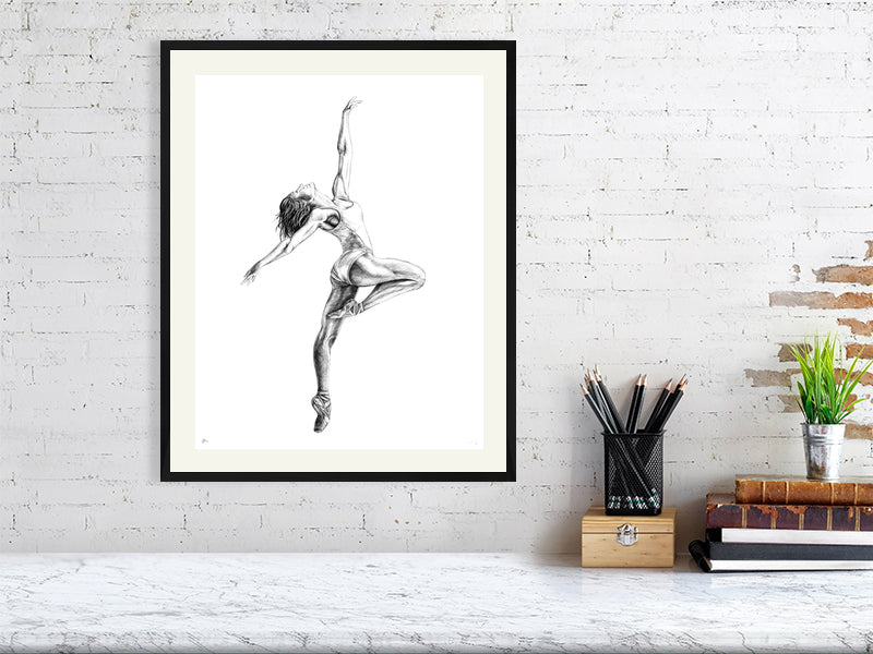 Large framed pencil drawing of a ballet dancer mid Pique pose, with arms outstretched, signed in the corner by Sophie Hall and hanging on a white wall over a marble desk.