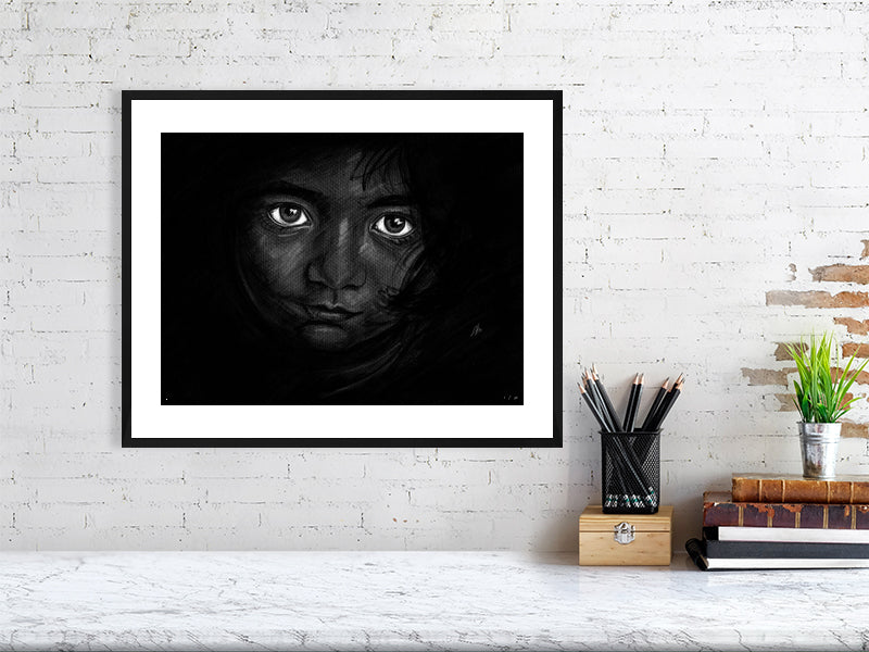 A large framed chalk and pencil portrait drawing on a dark background of a young child with striking emotive eyes, signed in the corner by Sophie Hall and hanging on a white brick wall.