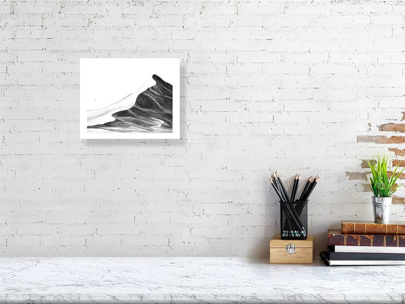 A small unframed pencil drawing of a vast sand dune with a caravan of camels climbing to the peak Signed on the left by Sophie Hall and hanging on a white brick wall above a desk.