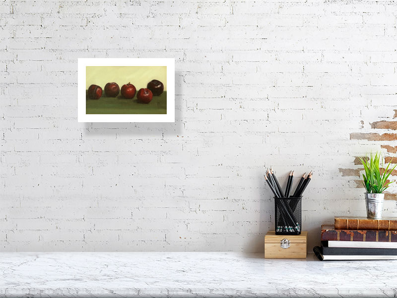A small giclee print oil painting still life of five ripe plums on a deep green cloth, signed by Sophie Hall and hanging on a white wall above a desk.
