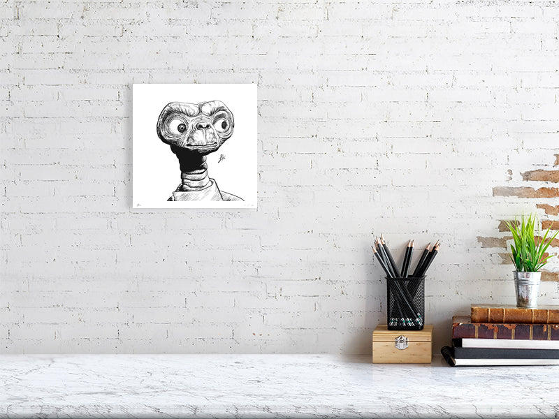A small square ink drawing of ET, hanging on a white brick wall above a desk.