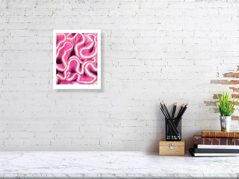 A small unframed artwork featuring vibrant coloured pencil illustration of pink and white brain coral, hanging on a white brick wall above a desk.