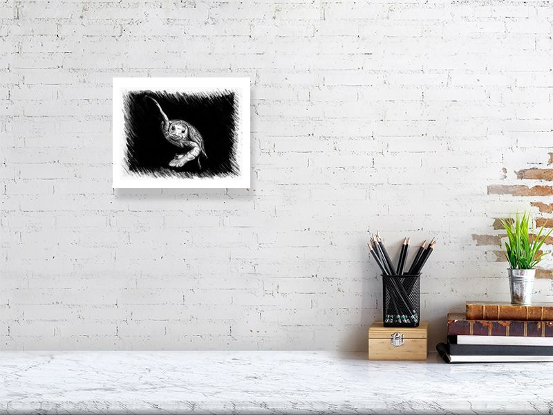 A small unframed pencil sketch of a swimming turtle on a black background, hanging on a white brick wall over a modern desk.
