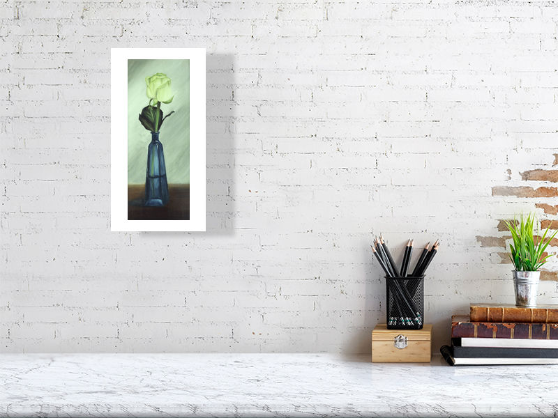 A small unframed print of White Rose in Blue Bottle, signed by the artist Sophie Hall and hanging on a white wall over a desk.