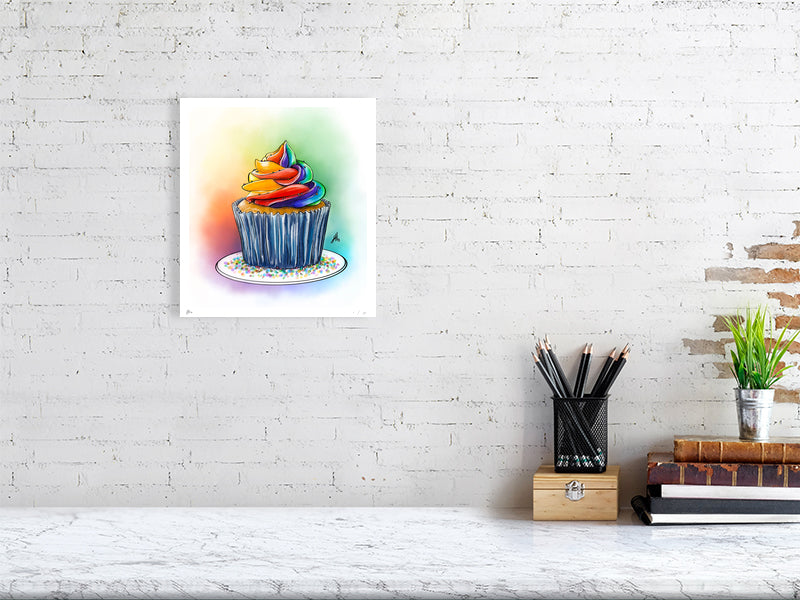 A small unframed print of Frost, by Sophie Hall: an artistic ink drawing of a cupcake topped with multi-colored frosting, depicted with vibrant pastel colours. The print hangs on a white brick wall.
