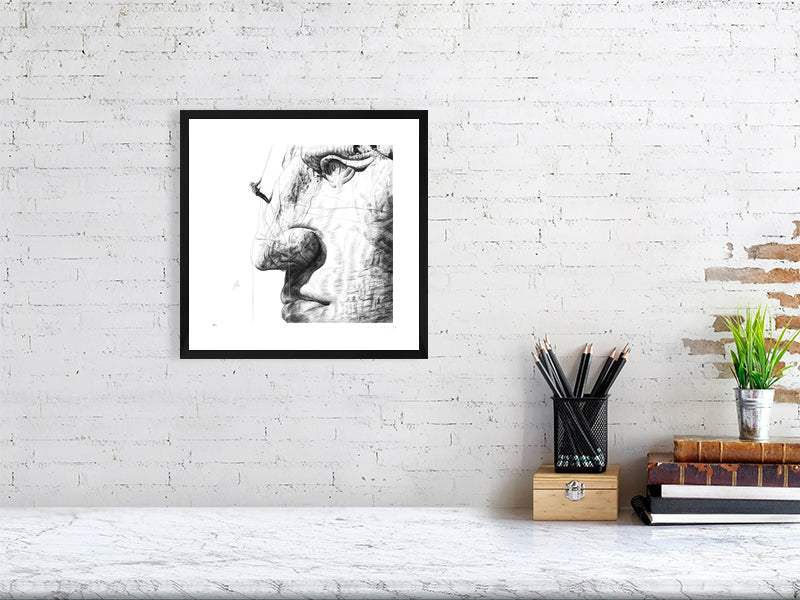 Framed pencil drawing of Crazy Horse monument hanging on a white brick wall above desk paraphernalia