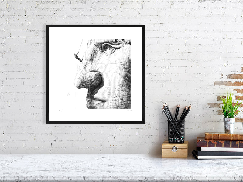 Framed pencil drawing of Crazy Horse monument hanging on a white brick wall above desk paraphernalia