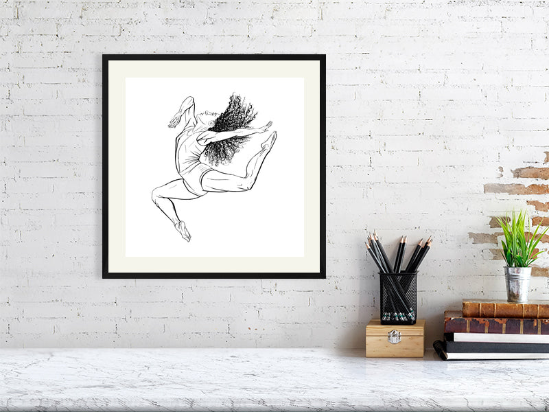 A large square framed ink drawing of a ballet dancer in mid-leap, signed by Sophie Hall and hanging on a white brick wall over a marble desk.