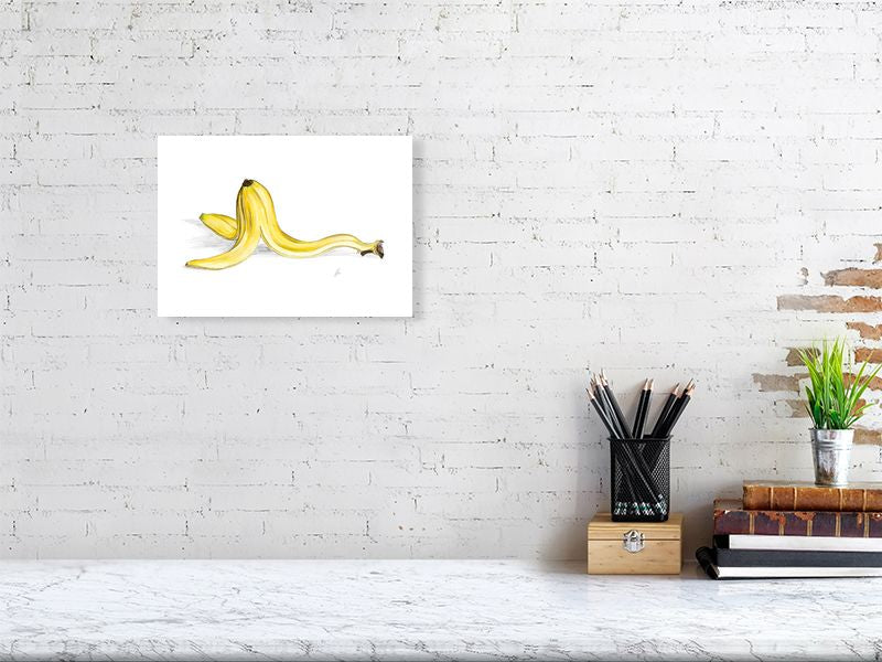 A small unframed watercolour and pencil illustration of a banana peel with a focus on realistic texture and colour, hanging on a white brick wall above a desk.