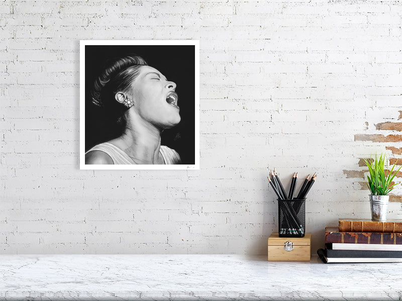 An unframed black and white portrait pencil drawing of Billie Holiday, depicting the singer with a expressive pose and closed eyes, capturing a sense of emotion and intensity. Hanging on a white brick wall over a desk.