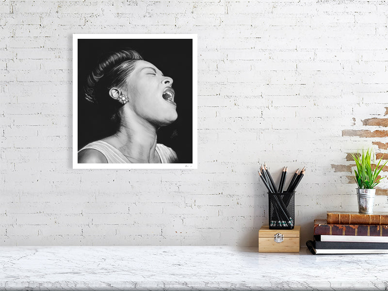 A large unframed black and white portrait pencil drawing of Billie Holiday, depicting the singer with a expressive pose and closed eyes, capturing a sense of emotion and intensity. Hanging on a white brick wall over a desk.