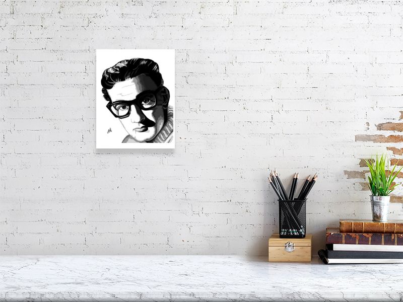 A small unframed ink portrait of Buddy Holly in sharp contrast monochrome, hanging on a white brick wall over a desk.