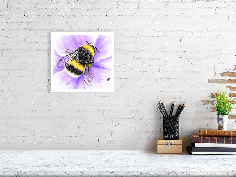A medium unframed watercolour realistic artwork of a fluffy yellow bumblebee on a purple flower, signed by Sophie Hall and hanging on a white brick wall over a desk.