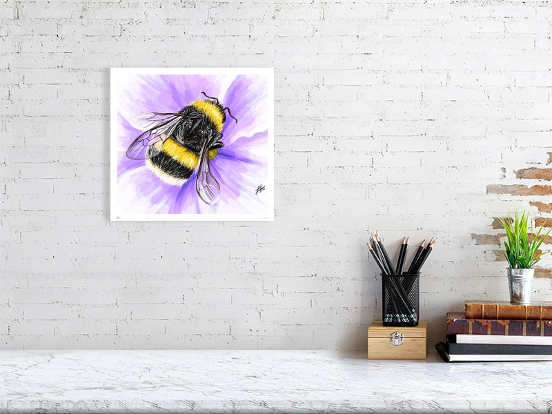 A large unframed watercolour realistic artwork of a fluffy yellow bumblebee on a purple flower, signed by Sophie Hall and hanging on a white brick wall over a desk.
