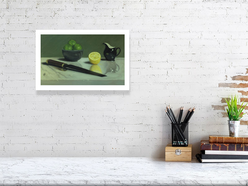 Medium size unframed print of a traditional style oil painting featuring citrus fruits in a bowl, a lemon cut in half, a black jug, and a knife placed on a reflective marble surface. Signed by the artist Sophie Hall and hanging on a white brick wall over a desk.