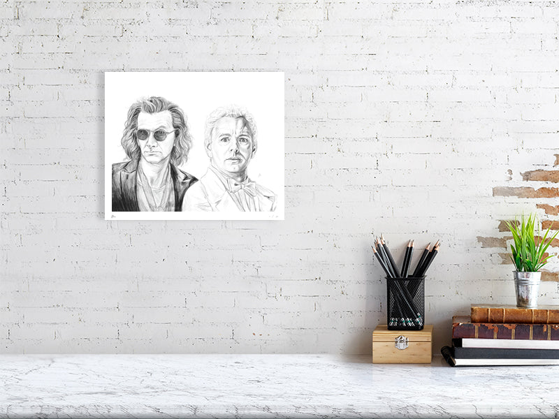 A medium unframed detailed pencil drawing of the characters Crowley and Aziraphale from the TV show Good Omens, signed by artist Sophie Hall and hanging on a white wall over a desk.