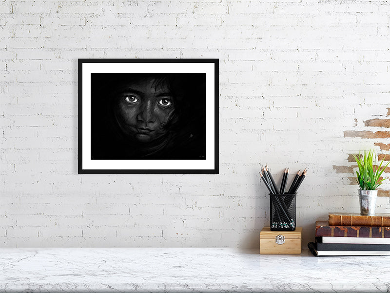 A medium framed chalk and pencil portrait drawing on a dark background of a young child with striking emotive eyes, signed in the corner by Sophie Hall and hanging on a white brick wall.