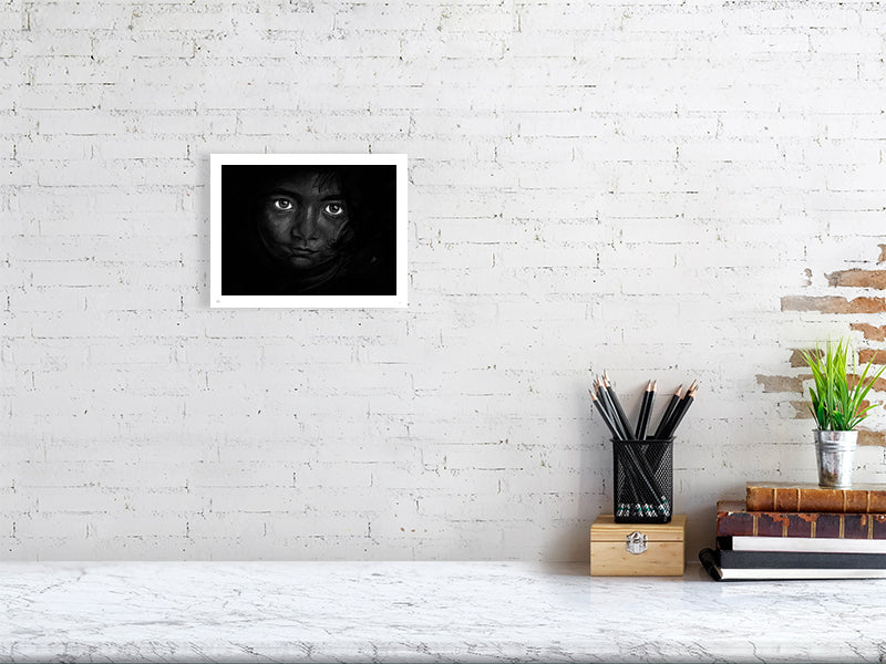 A small unframed chalk and pencil portrait drawing on a dark background of a young child with striking emotive eyes, signed in the corner by Sophie Hall and hanging on a white brick wall.