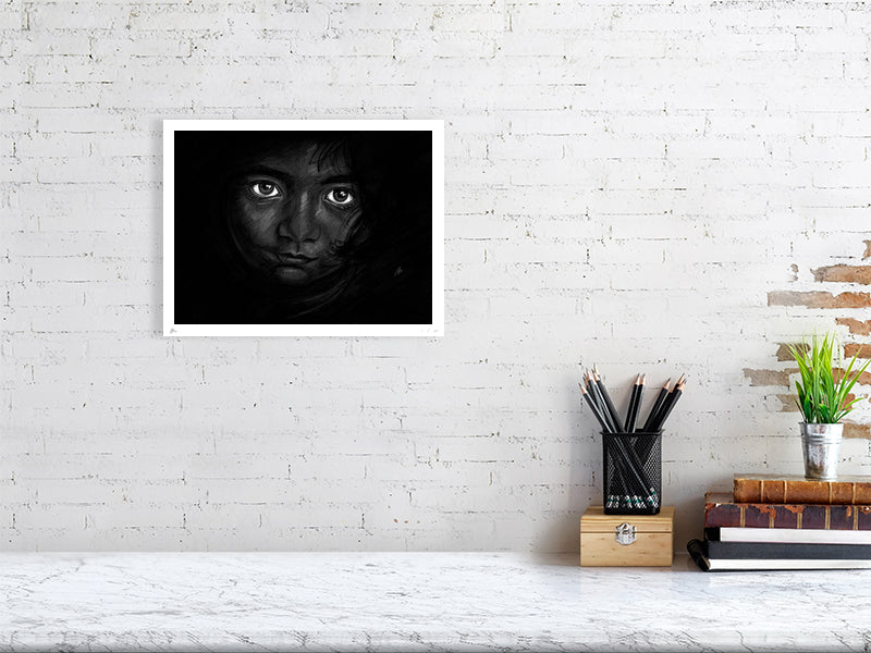 A large unframed chalk and pencil portrait drawing on a dark background of a young child with striking emotive eyes, signed in the corner by Sophie Hall and hanging on a white brick wall.
