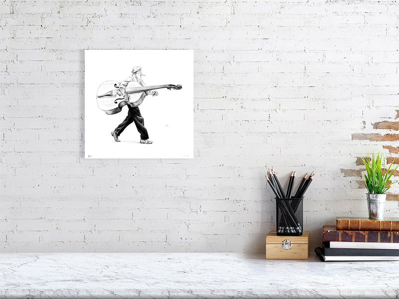 A small unframed pencil drawing of a man in a flat cap carrying a large bass instrument under one arm and striding towards the right. Artwork hangs on a white brick wall over a desk.
