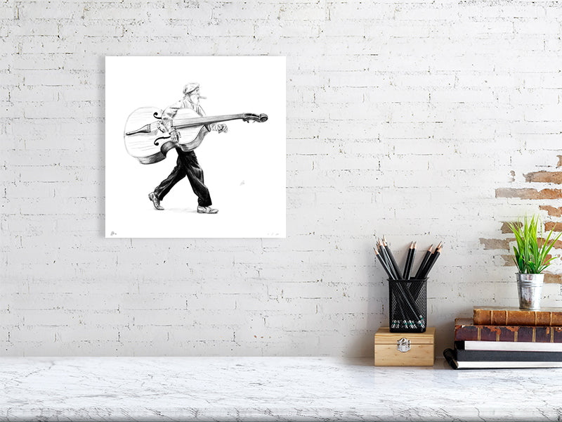 A medium size unframed pencil drawing of a man in a flat cap carrying a large bass instrument under one arm and striding towards the right. Artwork hangs on a white brick wall over a desk.
