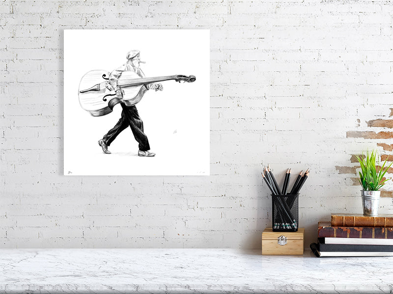 A large unframed pencil drawing of a man in a flat cap carrying a large bass instrument under one arm and striding towards the right. Artwork hangs on a white brick wall over a desk.