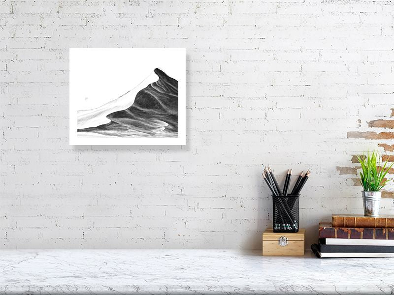 An unframed pencil drawing of a vast sand dune with a caravan of camels climbing to the peak Signed on the left by Sophie Hall and hanging on a white brick wall above a desk.