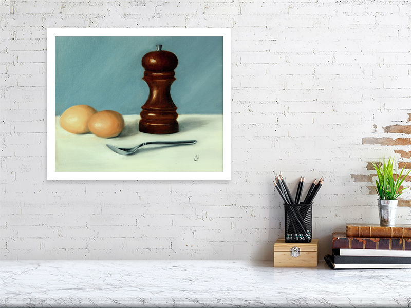A large unframed print of a still life oil painting featuring a wooden salt cellar, two eggs, and a spoon on a white surface, against a blue background, signed by the artist and hanging on a white brick wall.
