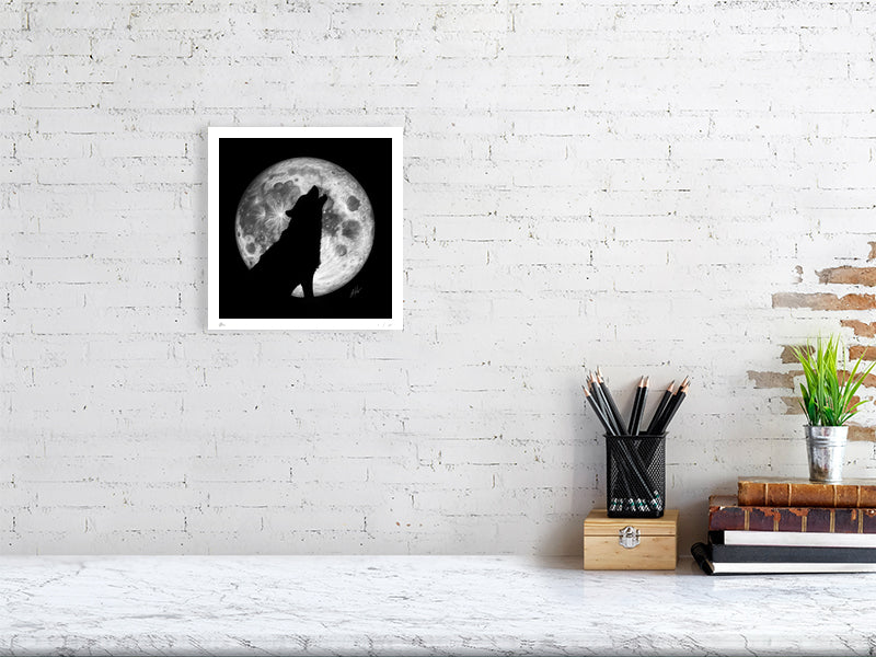 A small unframed pencil drawing of a wolf howling at the moon, with the outline of the wolf silhouetted by the a large full moon behind. Hanging on a white brick wall over a desk.