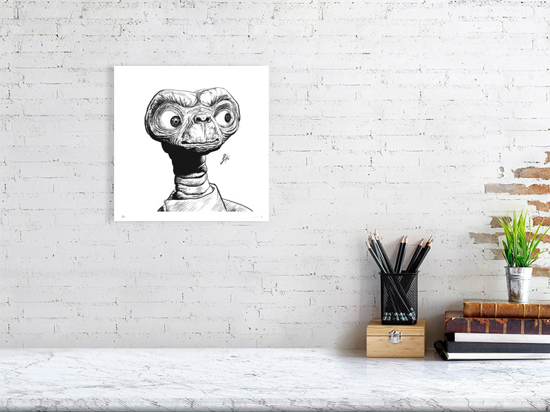 An unframed square ink drawing of ET, hanging on a white brick wall above a desk.