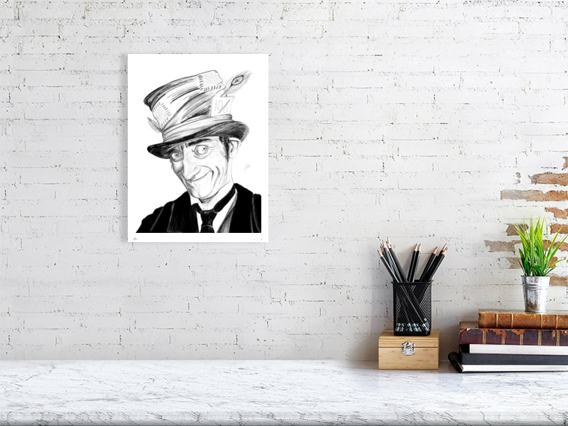 A medium size unframed print of a pencil portrait drawing featuring actor Marty Feldman as the Mad Hatter. Signed by Sophie Hall and hanging on a white brick wall over a desk.