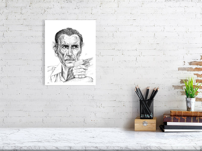 A medium unframed pencil drawing of Christopher Lee as Antonin Scaramanga from The Man with the Golden Gun. Signed by Sophie Hall and hanging on a white brick wall over a desk.