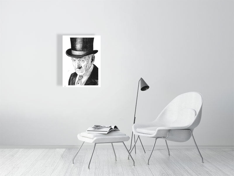 A small unframed black and white pencil drawing of Ian McKellen wearing a black top hat. Signed with Sophie Hall's monogram and hanging on a white wall above a white armchair, footrest and lamp.