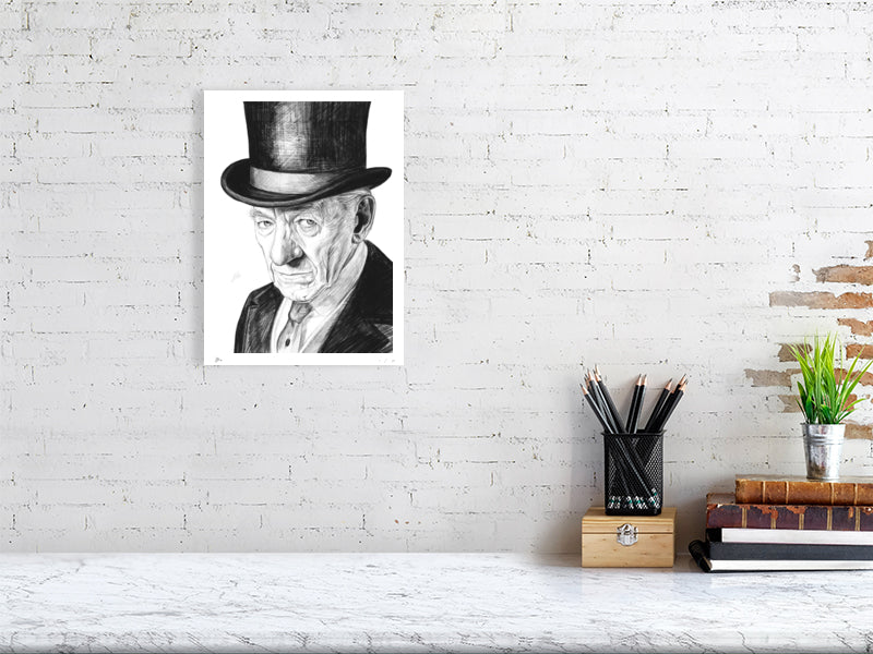 A medium size unframed pencil drawing of Ian McKellen wearing a black top hat as Sherlock Holmes. Signed with Sophie Hall's monogram and hanging on a white wall above a desk.