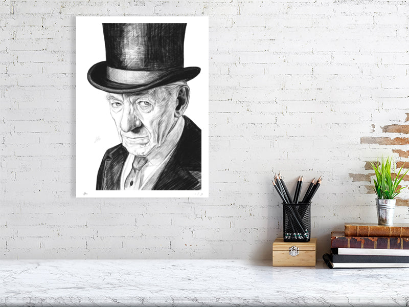 A large unframed pencil drawing of Ian McKellen wearing a black top hat as Sherlock Holmes. Signed with Sophie Hall's monogram and hanging on a white wall above a desk.