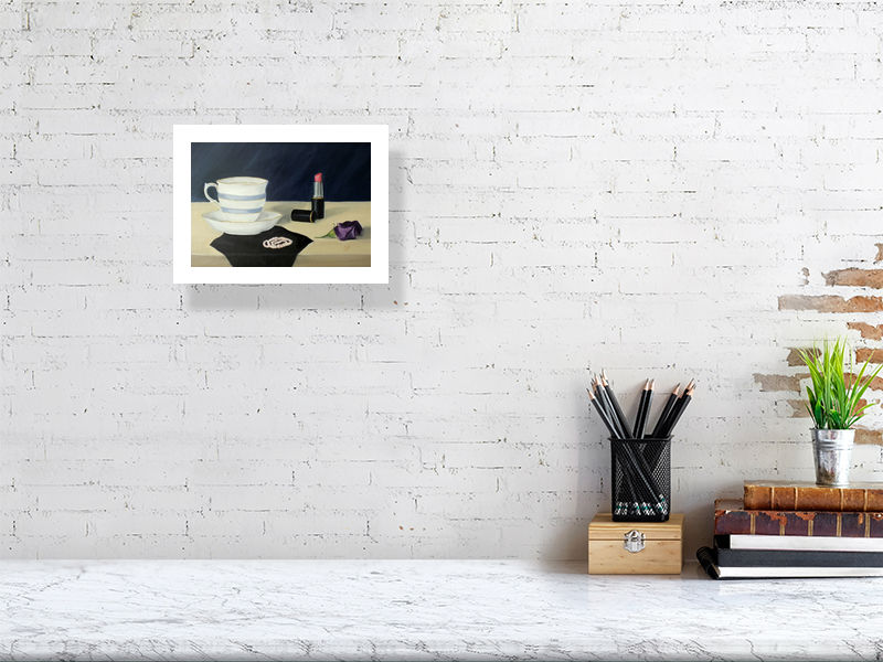 A small giclee print featuring an oil painting scene with a teacup, saucer, lipstick, and a purple flower on a dressing table. Signed by Sophie Hall and hanging on a white brick wall over a desk.