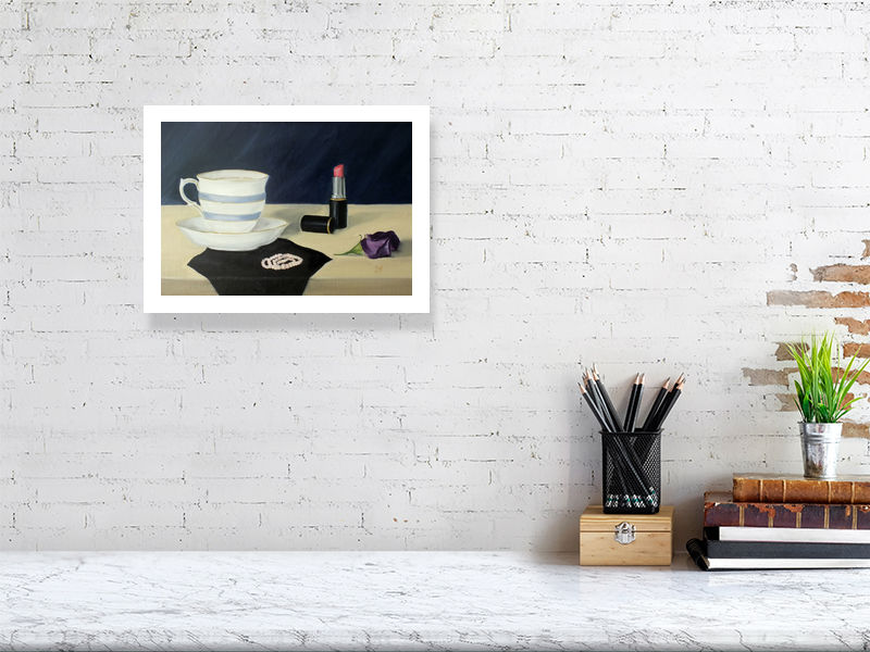 A mid size giclee print featuring an oil painting scene with a teacup, saucer, lipstick, and a purple flower on a dressing table. Signed by Sophie Hall and hanging on a white brick wall over a desk.