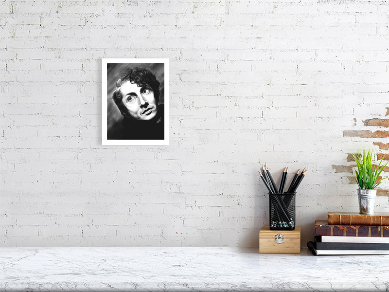 A small unframed black and white pencil drawing of Quentin Crisp, featuring expressive facial features and a direct gaze. Hanging on a white brick wall over a desk.