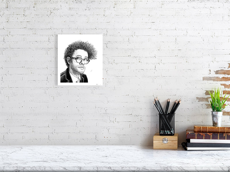 A small unframed pencil drawing portrait of Richard Ayoade, hanging on a white brick wall over a marble desk.