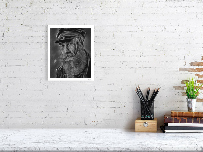 A small unframed pencil and chalk portrait drawing of an old sailor in monochrome with a grey background, hanging on a white brick wall over a desk.