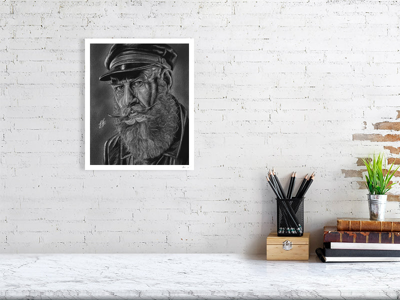 A medium unframed pencil and chalk portrait drawing of an old sailor in monochrome with a grey background, hanging on a white brick wall over a desk.