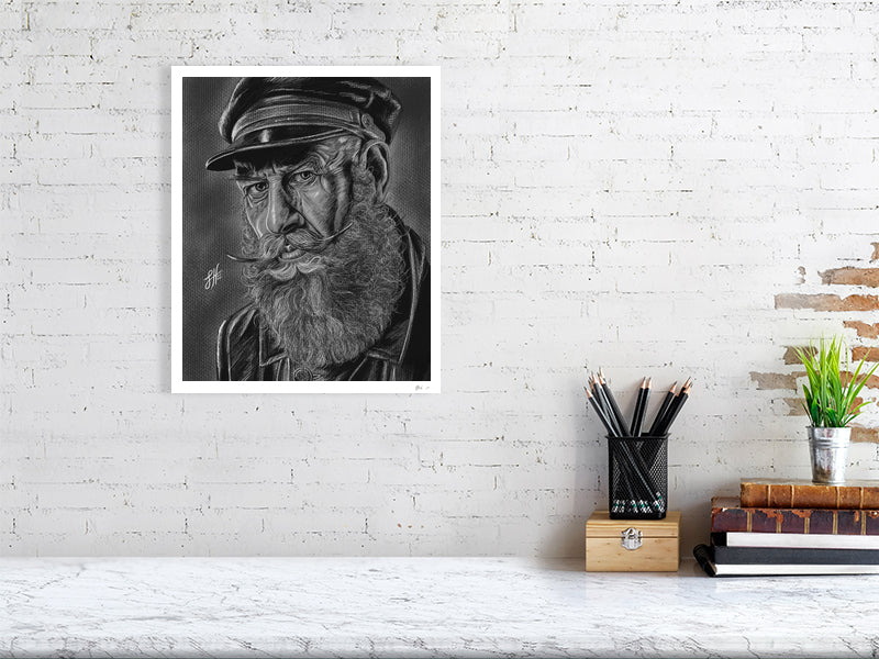 A large unframed pencil and chalk portrait drawing of an old sailor in monochrome with a grey background, hanging on a white brick wall over a desk.