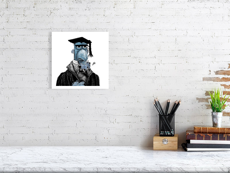 A medium size unframed print hanging on a white brick wall above a desk. The artwork features a detailed ink drawing of Sam the blue Eagle from the Muppets Christmas Carol, wearing a black coat, white shirt, and black teacher mortar board hat. Monogram signed by Sophie Hall.
