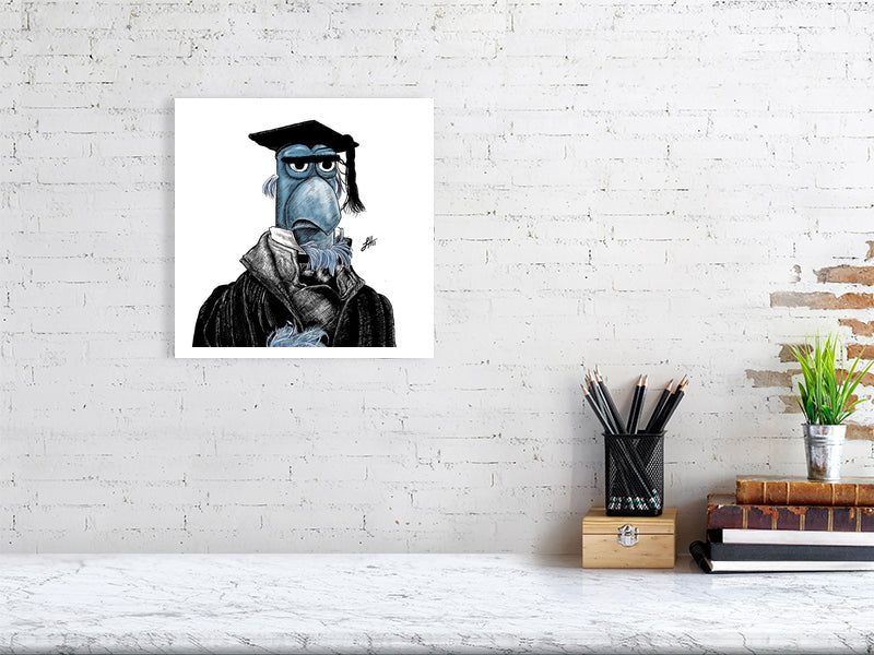 A large unframed print hanging on a white brick wall above a desk. The artwork features a detailed ink drawing of Sam the blue Eagle from the Muppets Christmas Carol, wearing a black coat, white shirt, and black teacher mortar board hat. Monogram signed by Sophie Hall.