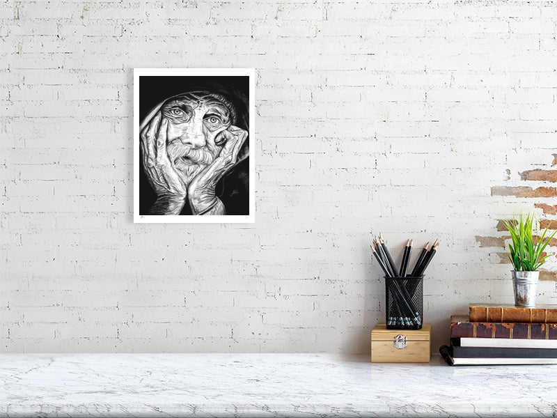 A medium size unframed pencil portrait depicting an elderly man with his chin in his hands and a contemplative expression. Print hangs on a white brick wall above a desk.