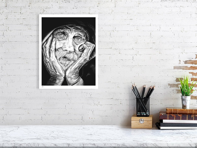 A large unframed pencil portrait depicting an elderly man with his chin in his hands and a contemplative expression. Print hangs on a white brick wall above a desk.