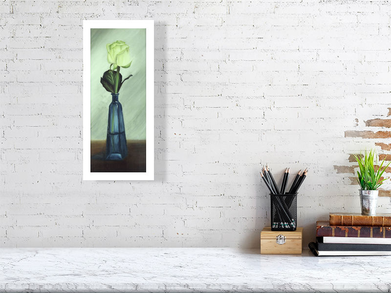 A medium size unframed print of White Rose in Blue Bottle, signed by the artist Sophie Hall and hanging on a white wall over a desk.